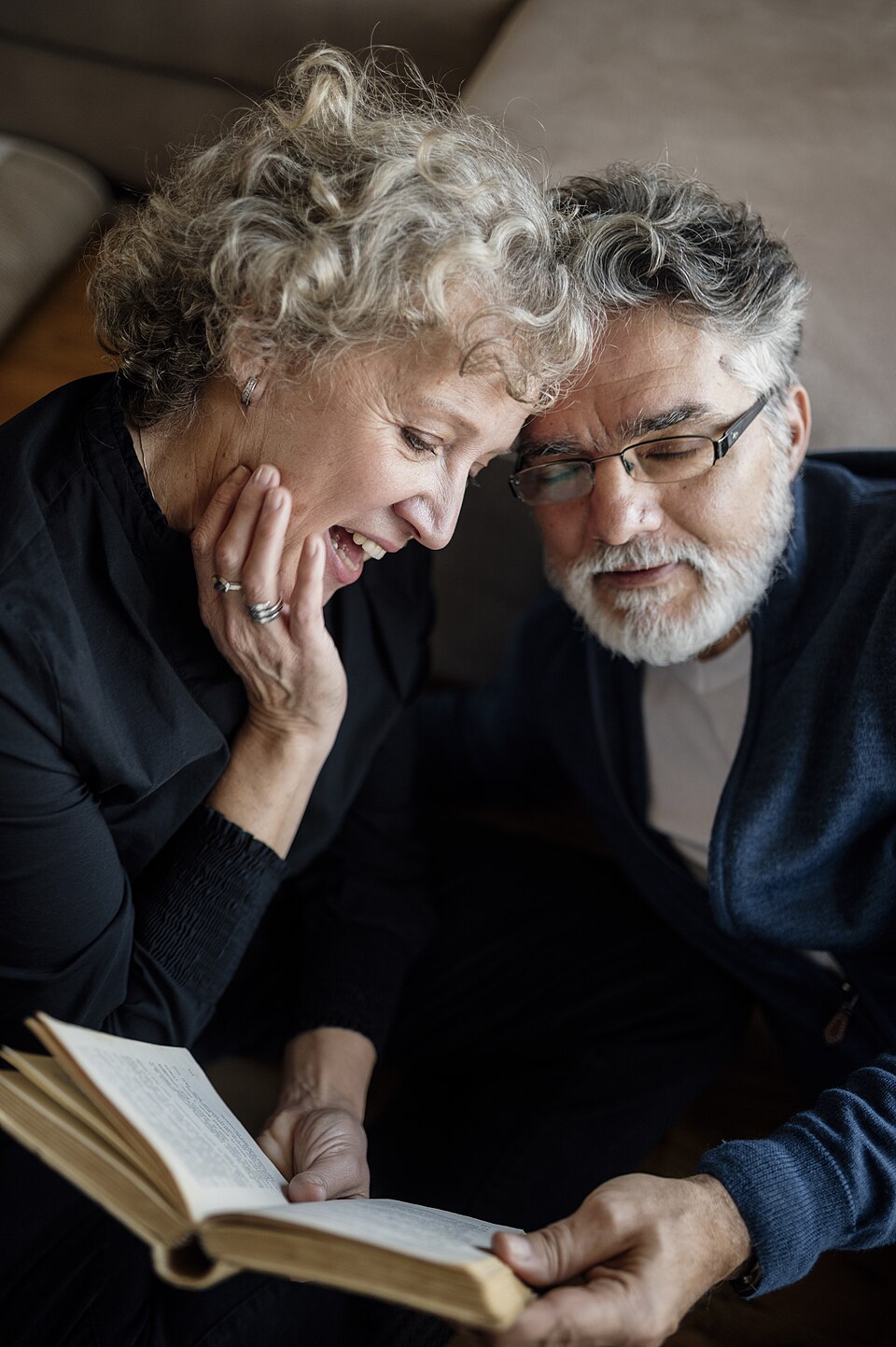 An older couple laughing together while reading a book at home